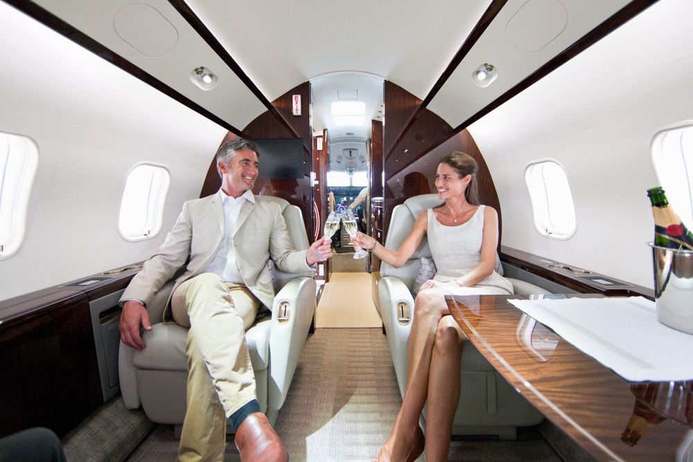 A close up of a smiling, affluent couple drinking champagne on a private jet.