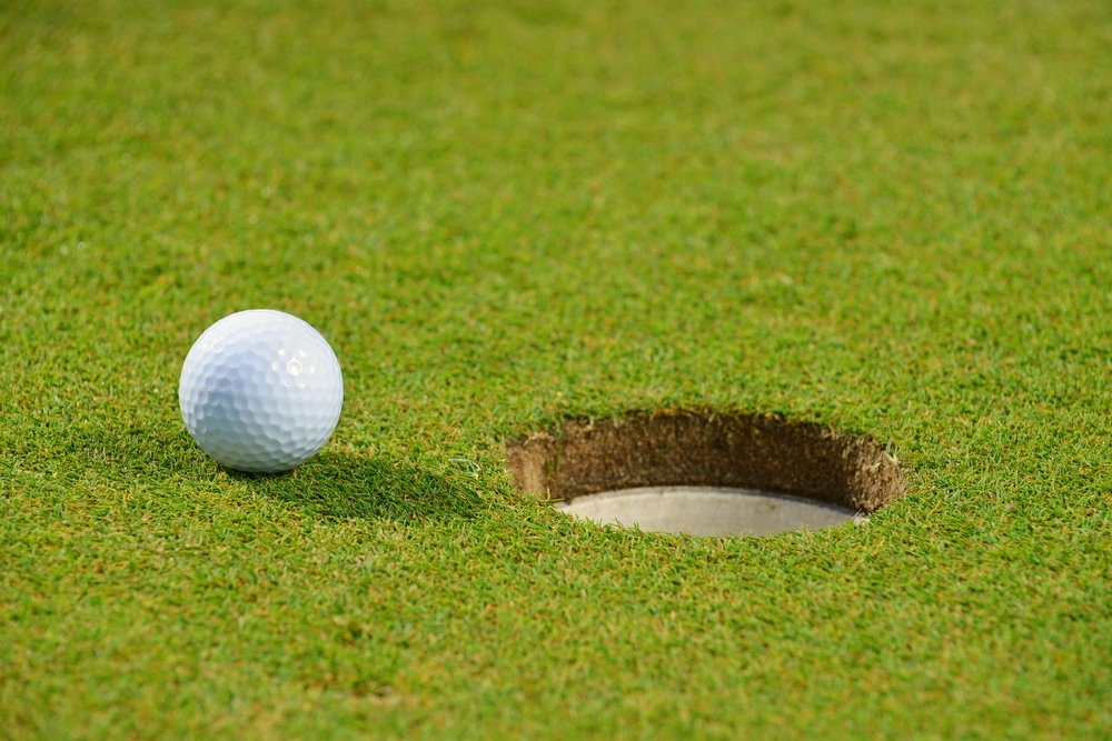 A golf ball rolls towards the hole.