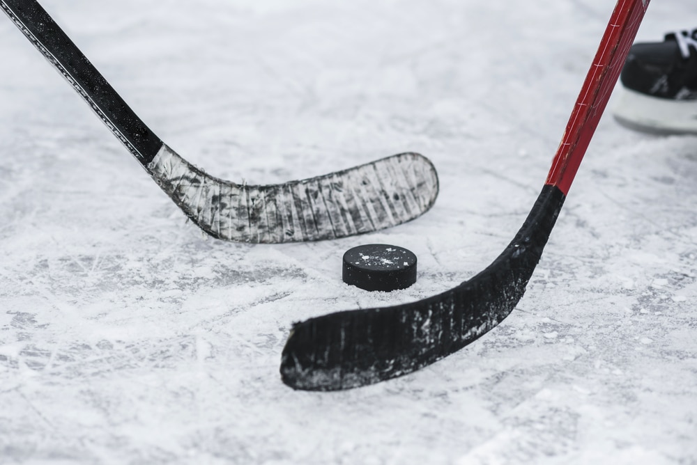A close up of two hockey sticks battling over a hockey puck.