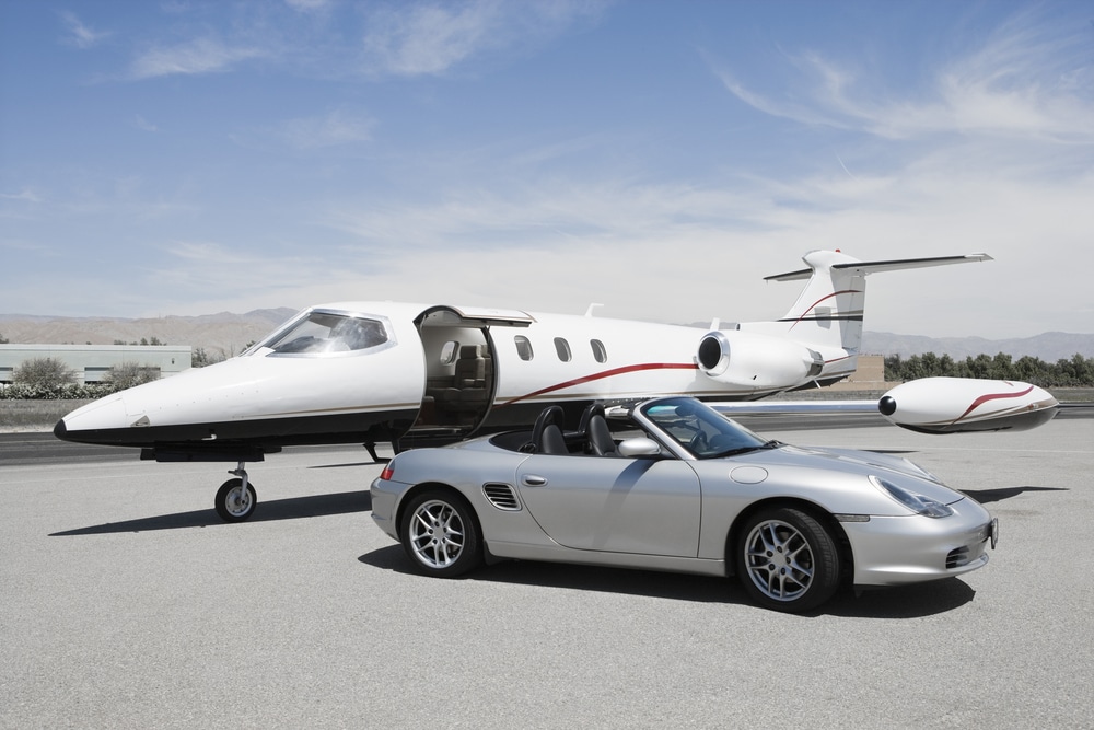 A grey Porsche convertible sits on the runway beside a private jet charter.
