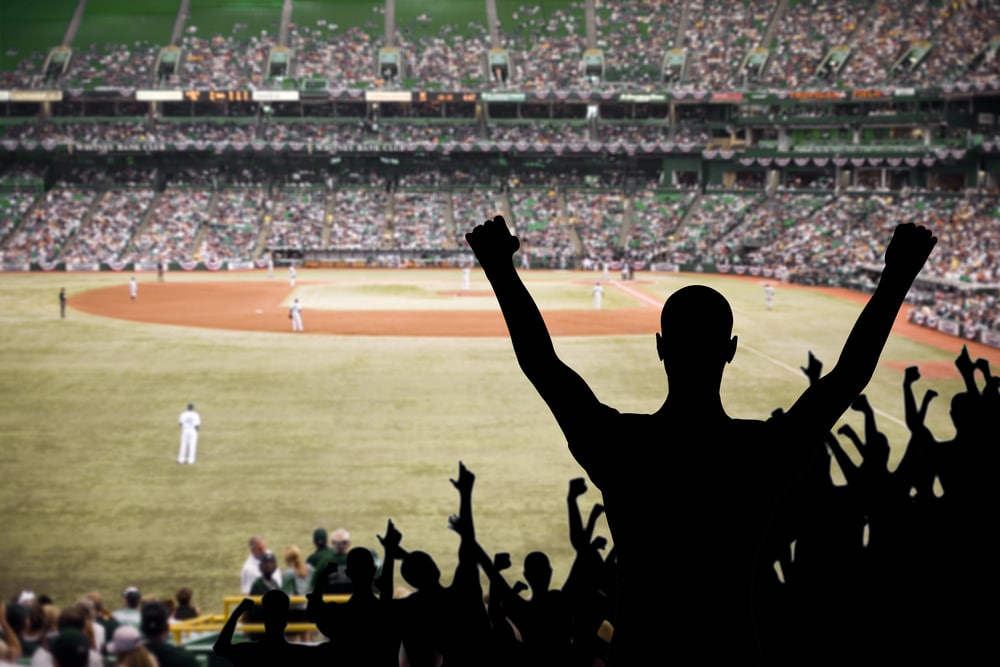 A silhouette of a baseball fan cheering in front of a baseball diamond.