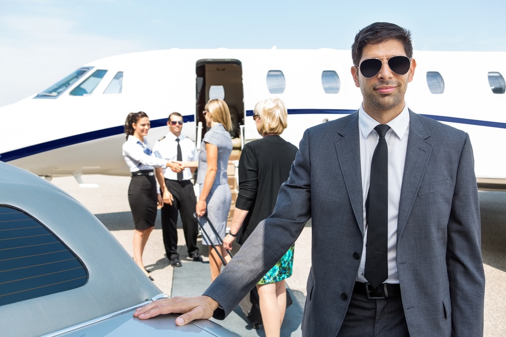 A man leans against a limo in front of a private jet.