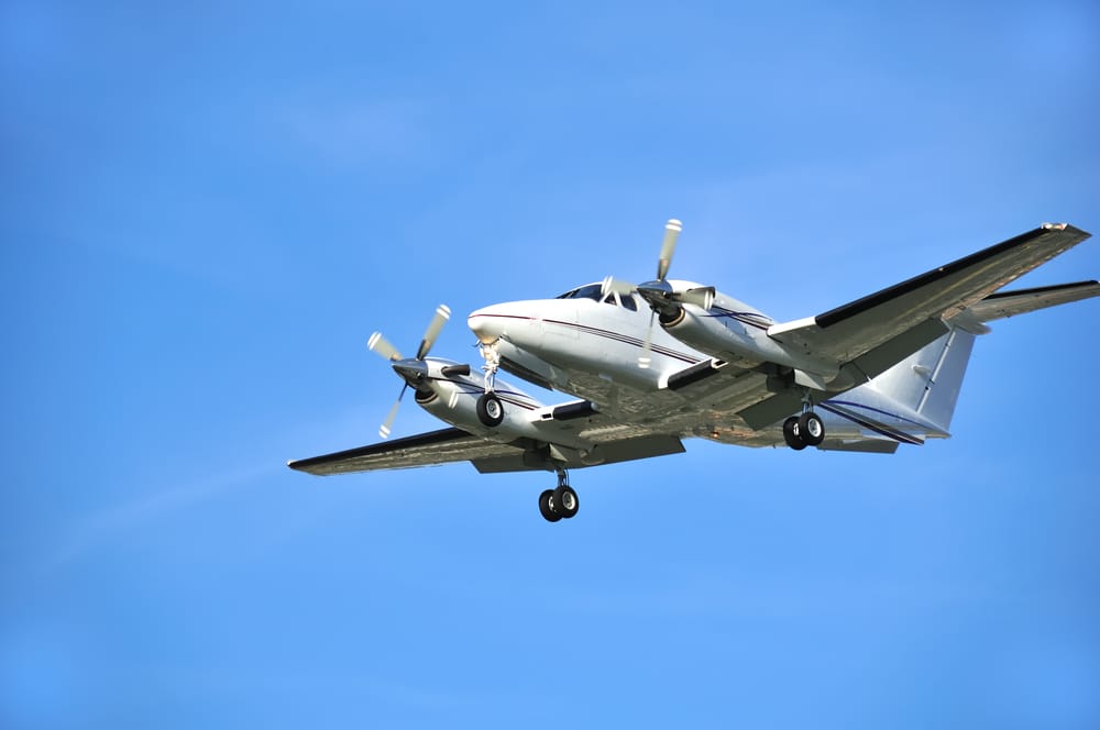 A twin turboprop plane soars through the air against a backdrop of a blue sky.