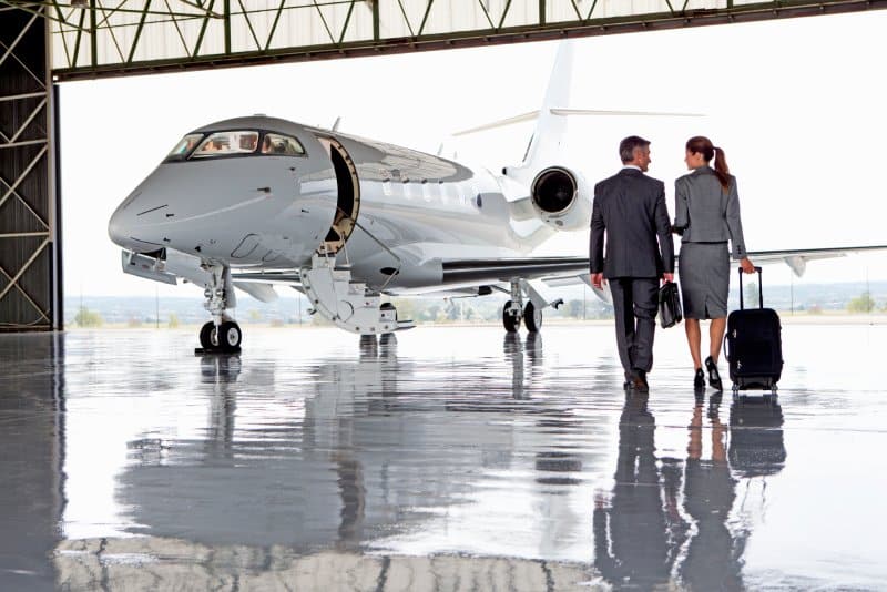 Two business people, a man and a woman, walking toward a private jet in a hangar.