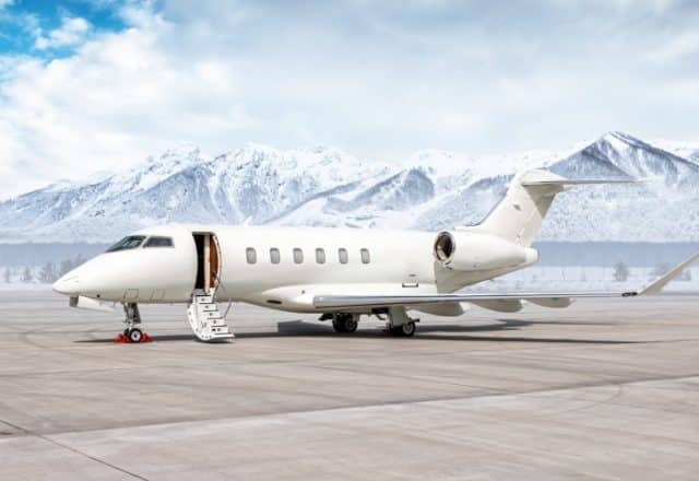 A private jet sits parked on a runway with snow-capped mountains in the background