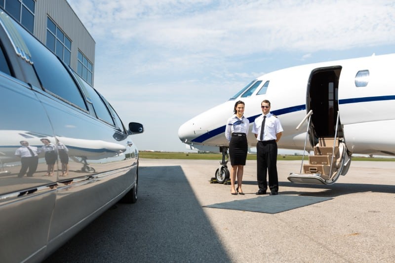 Flight attendant and pilot standing neat limousine and private jet at airport terminal