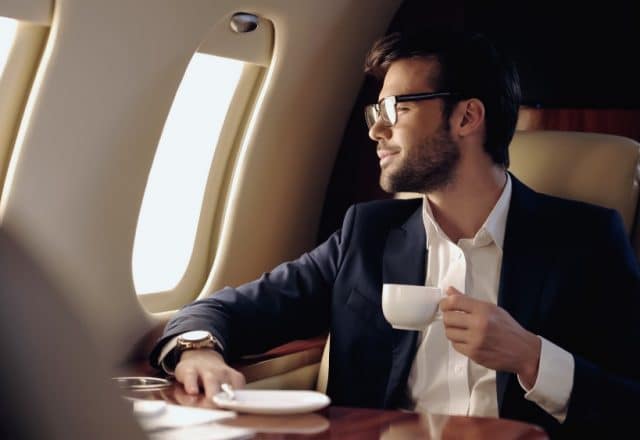Smiling businessman holding cup and looking at window in private plane