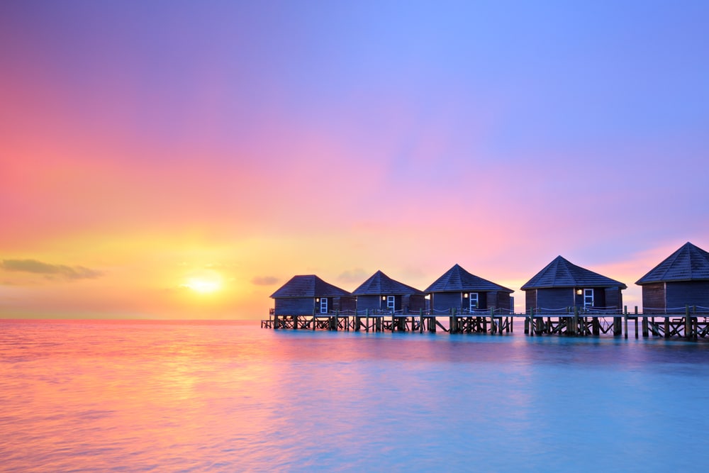 The sun sets above overwater bungalows in the Maldives.