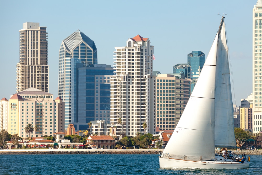 A sail boat cruises past the downtown San Diego skyline on a sunny day.