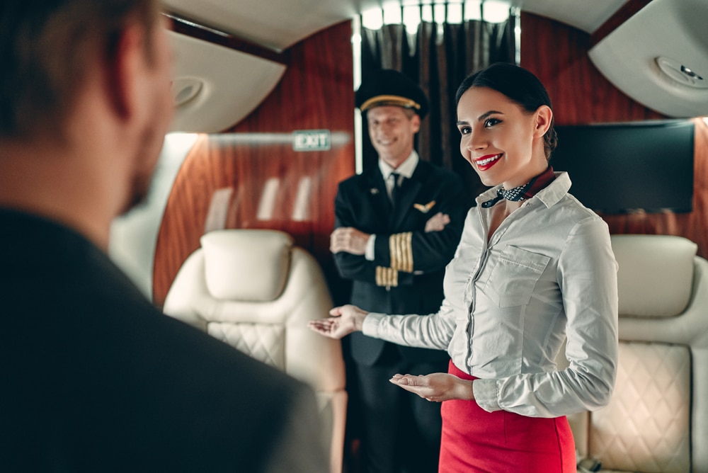 A private jet crew greets a passenger as they board the aircraft.