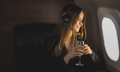 A woman wearing headhpones enjoys a glass of wine while looking out the window of her private jet.
