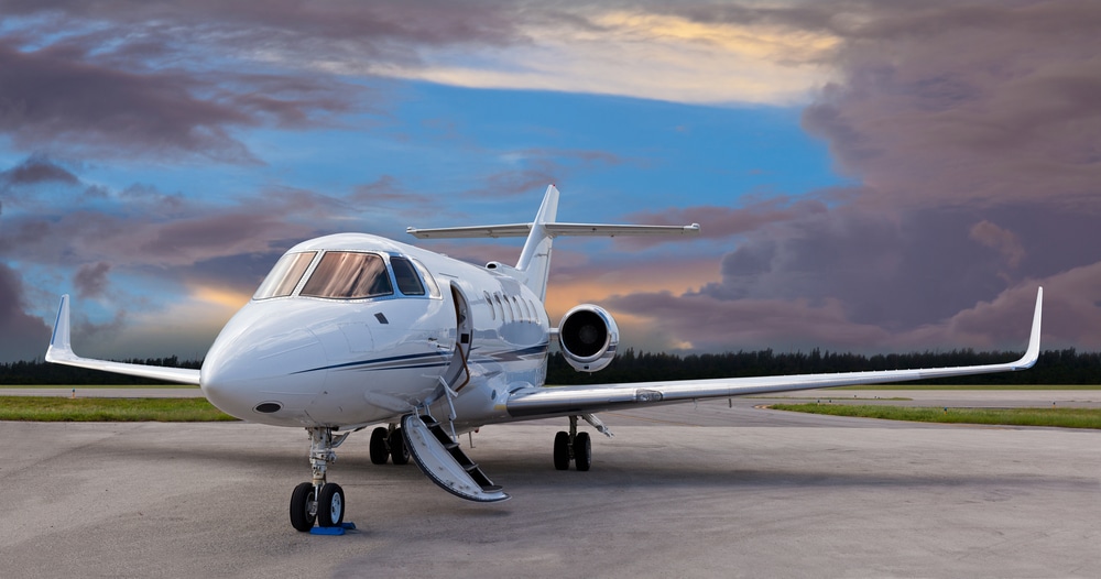 A private jet sits on the tarmac with the doors open against a backdrop of a beautiful summer sunset.