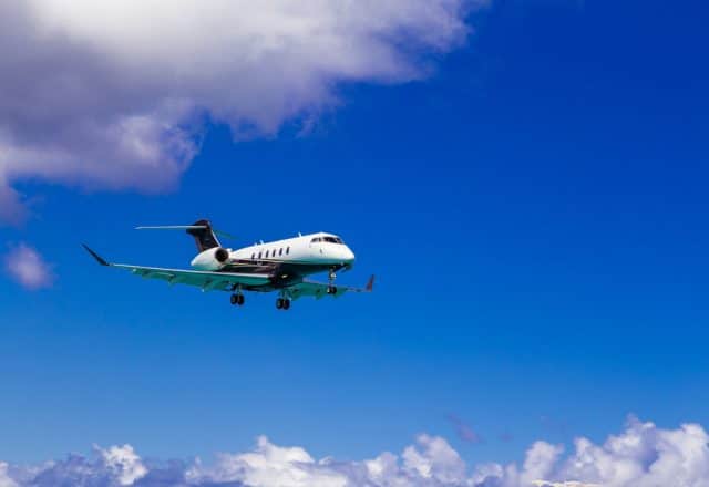 A luxury private jet flies through the sky on a clear, sunny day.