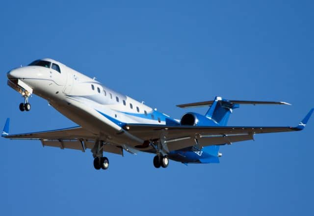 An Embraer Legacy 600 soars across a bright blue sky.