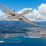 A small private plane soaring above a Spanish coastal city.