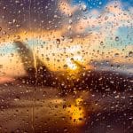 Rain on a window overlooking a jet at an airport during sunset.