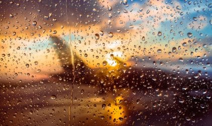 Rain on a window overlooking a jet at an airport during sunset.