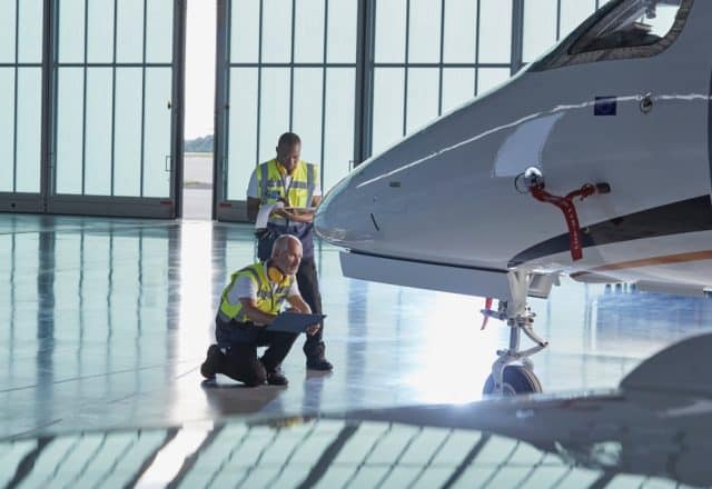 Technicians examine a private jet in a hangar.