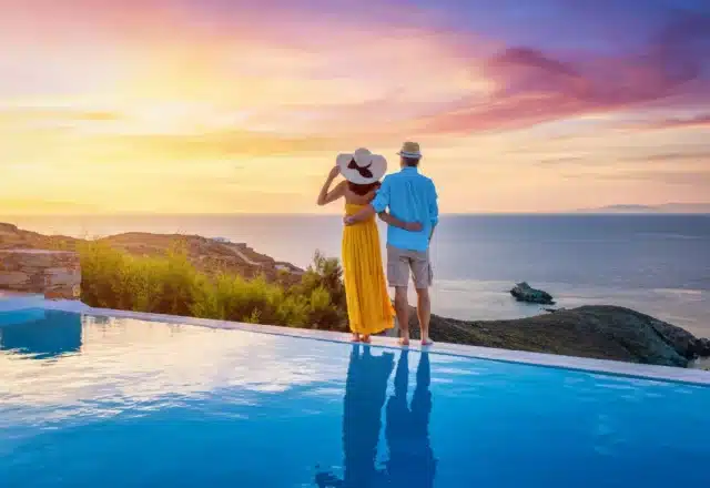 A honeymooning couple stands on the edge of an infinity pool, looking at the ocean.