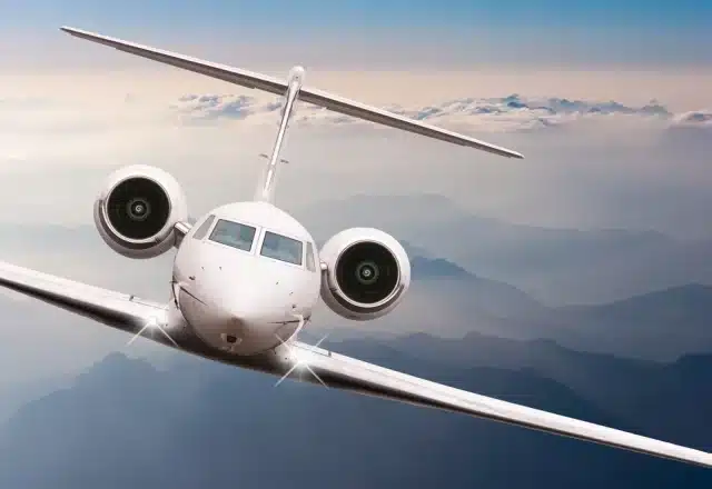 A head-on view of a charter jet soaring above the clouds.