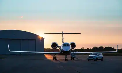 A luxury car parked next to a private jet at sunset.