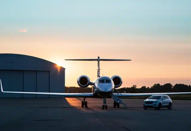 A luxury car parked next to a private jet at sunset.