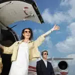 A smiling woman waving from the steps of a private jet.