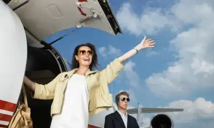 A smiling woman waving from the steps of a private jet.