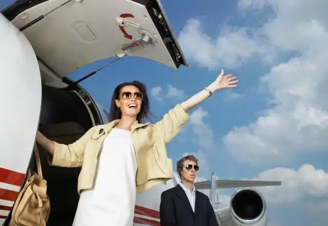 A smiling woman waving from the steps of a private jet.